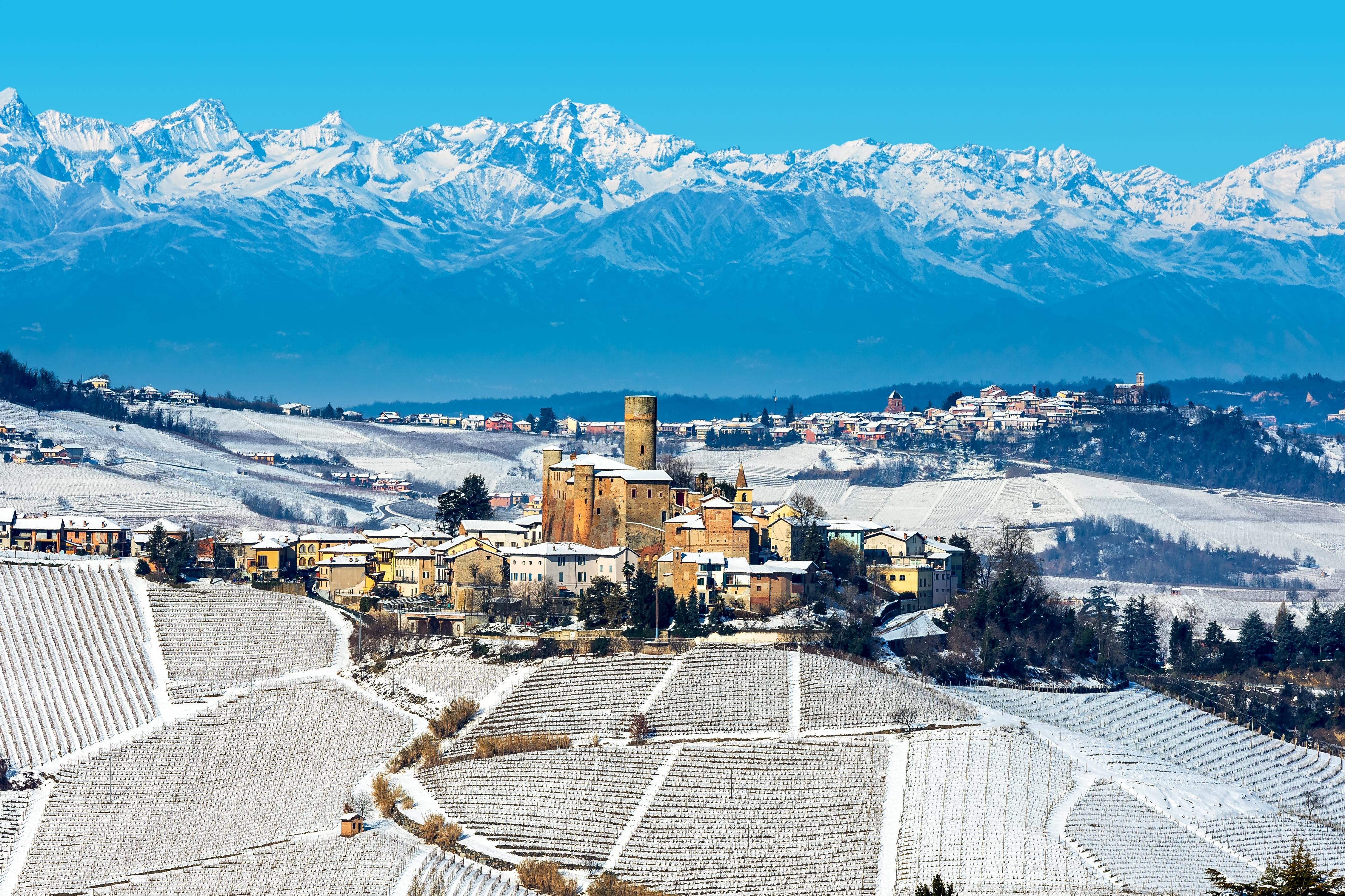 View of small medieval town on the hill covered with snow as mountains on background in the winter in Piedmont, Northern Italy