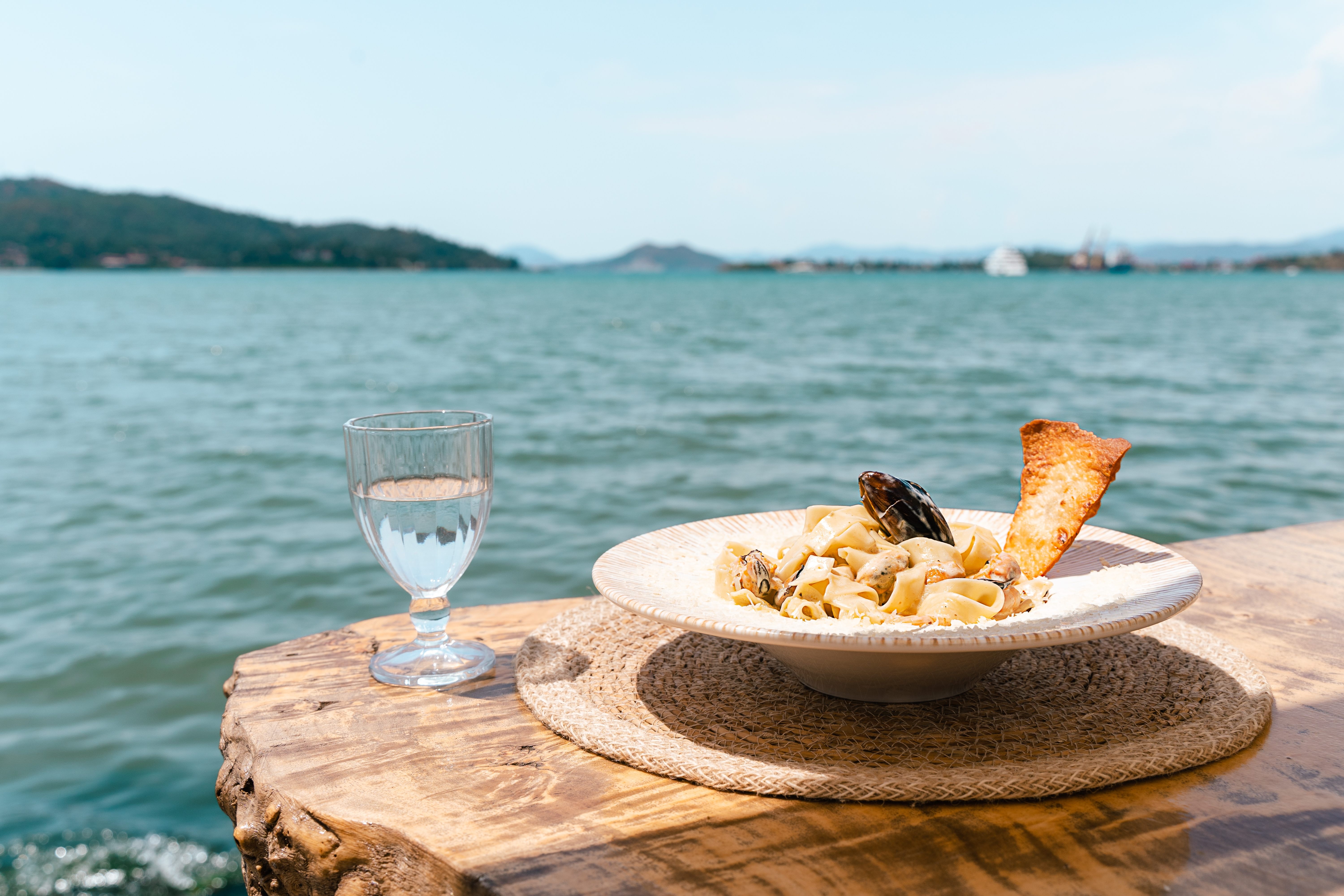 Seafood pasta spaghetti and a glass of water standing on a wooden table in outside cafe restaurant with scenery sea in the background