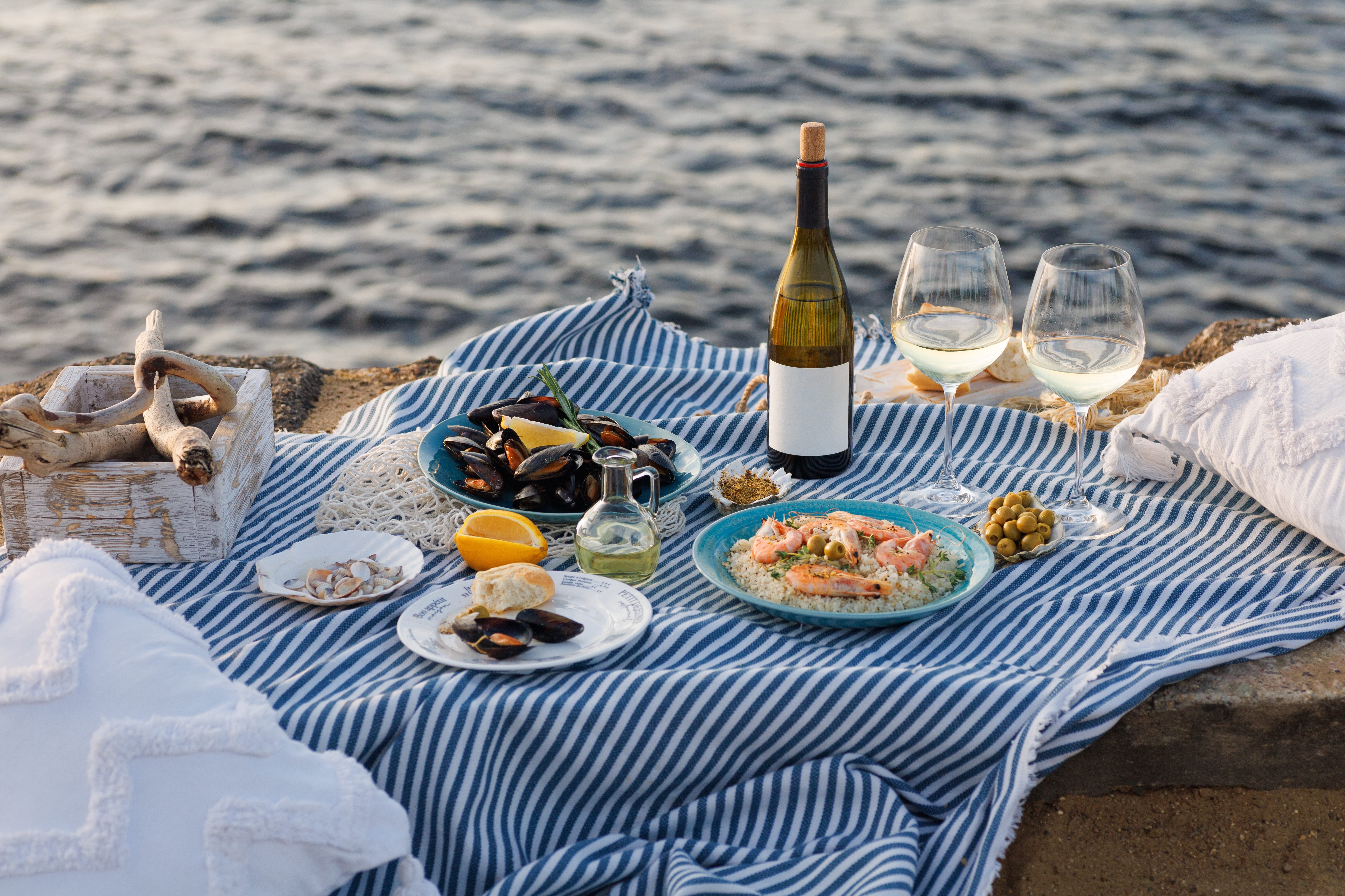 Seafood and wine on a low table covered with a blue and white tablecloth on the beach