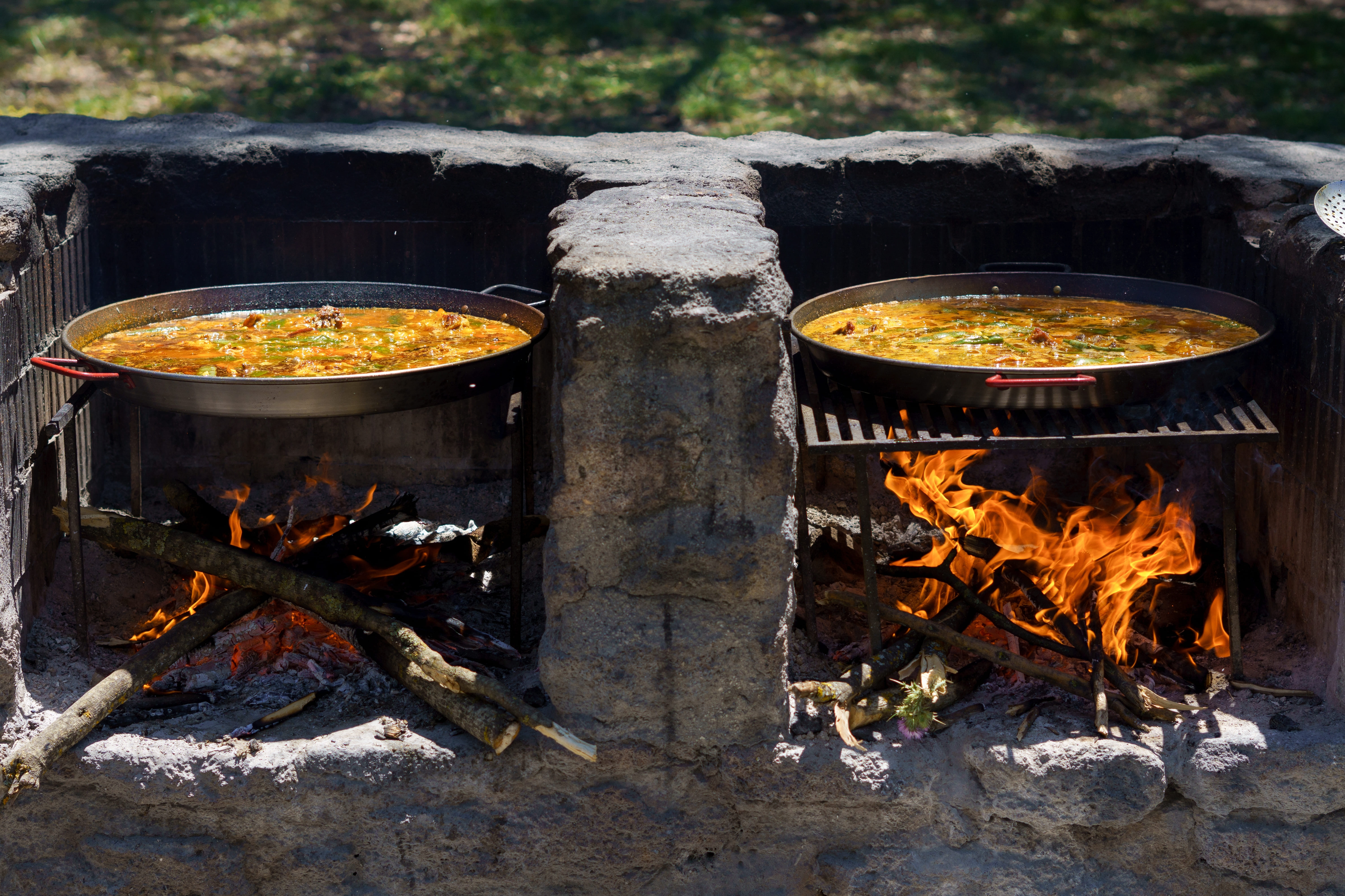 Close-up of two paella pans cooking a typical paella from Valencia, Spain on a barbecue in the countryside.